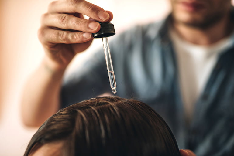 Hairstylist using a dropper to apply coconut oil to hair