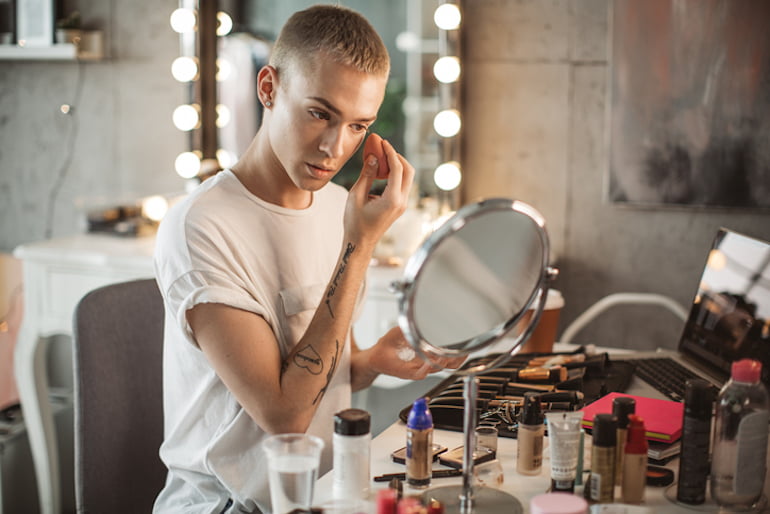 Young man applying foundation at his vanity, wondering what happens if you use expired makeup